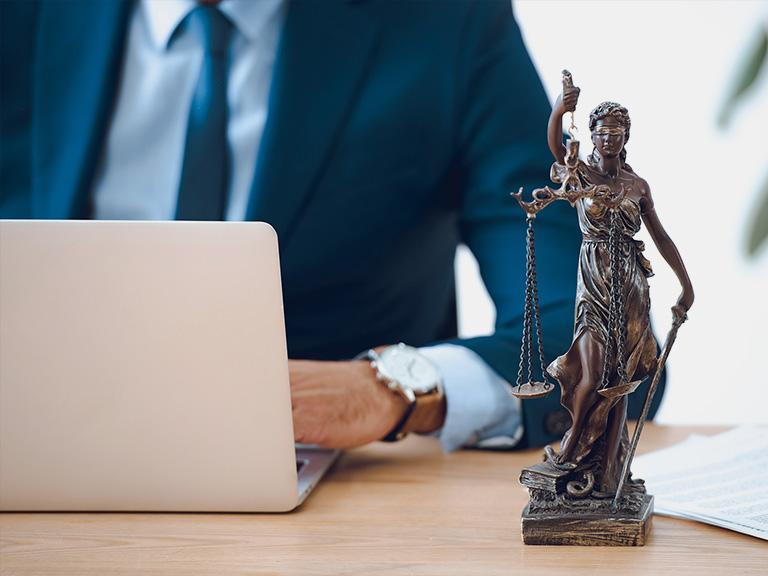 Figurka temidy na tle adwokata używającego laptopa